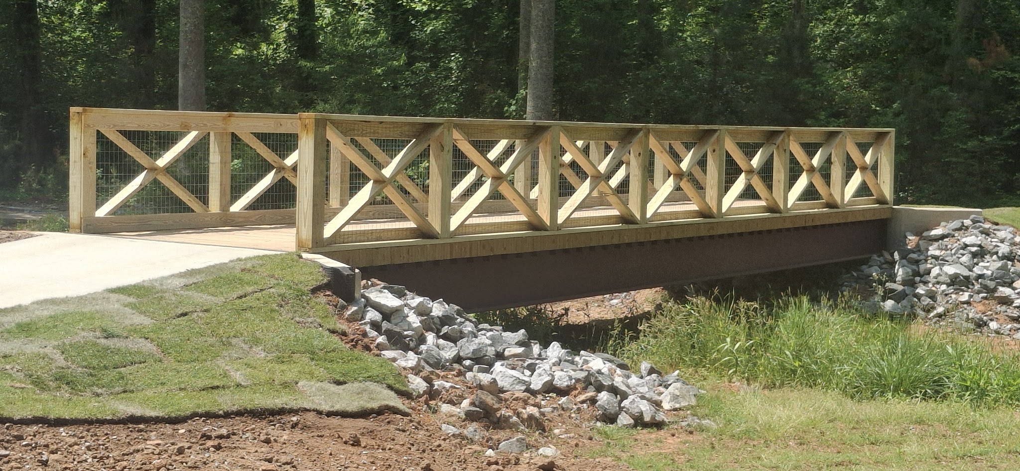 Wood bridge railing with crossed supports and wire mesh over a creek bed